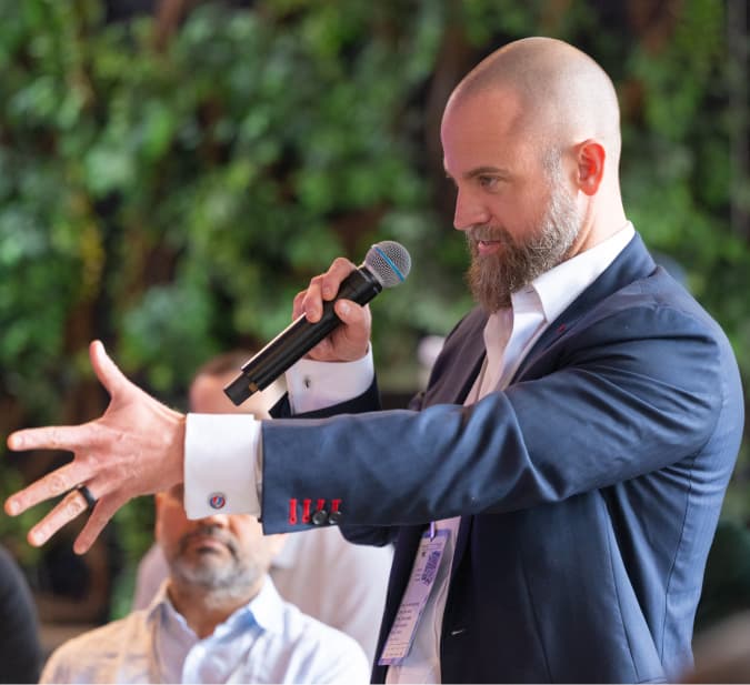 A speaker gesturing while addressing the Dirty Jobs Summit crowd